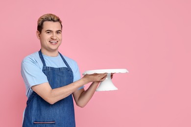 Photo of Portrait of happy confectioner holding cake stand on pink background, space for text