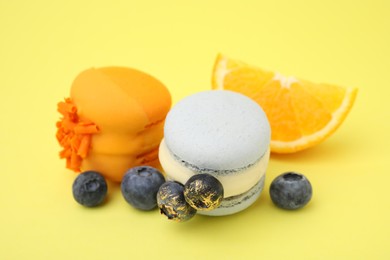 Photo of Delicious macarons, blueberries and orange slice on yellow background, closeup