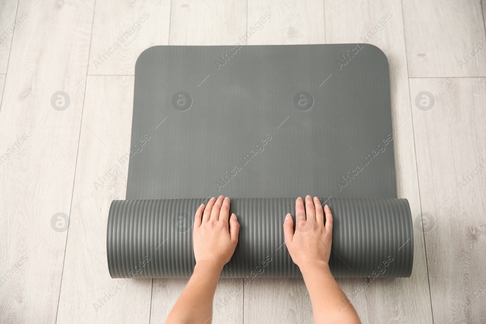 Photo of Woman rolling yoga mat on floor indoors, top view