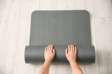 Photo of Woman rolling yoga mat on floor indoors, top view