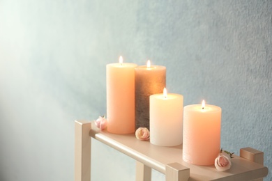 Photo of Candles with floral decor on table against color background