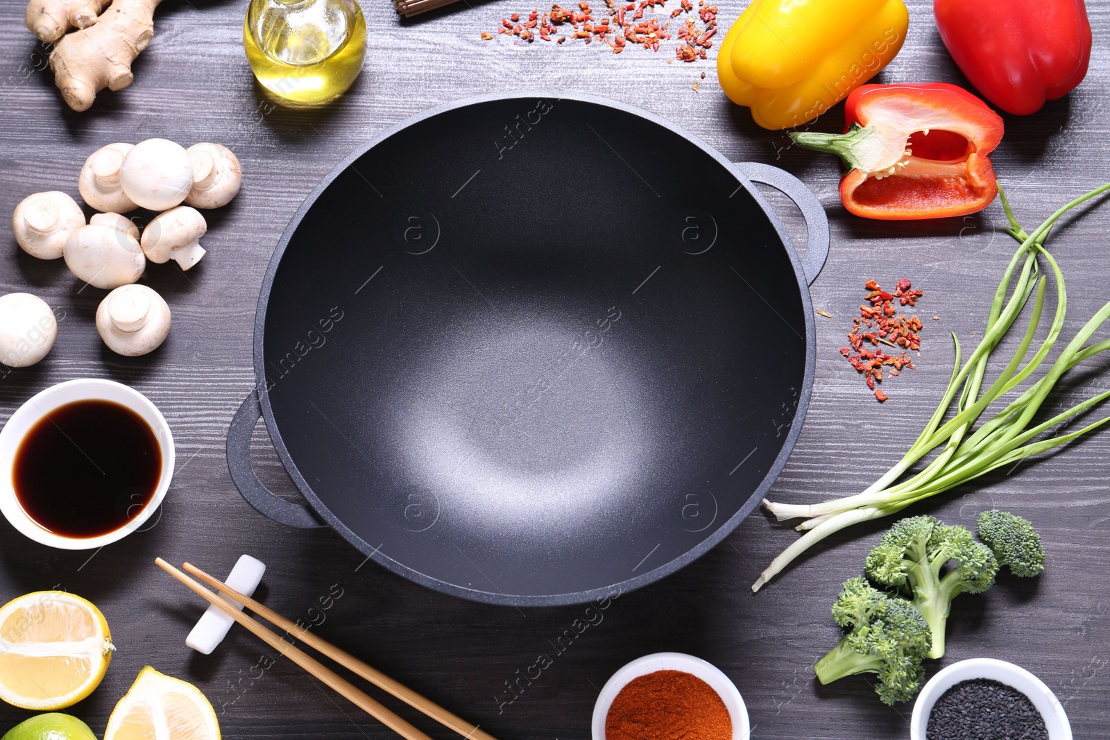 Photo of Empty iron wok and chopsticks surrounded by ingredients on dark grey wooden table