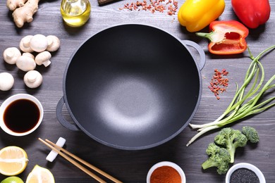 Photo of Empty iron wok and chopsticks surrounded by ingredients on dark grey wooden table