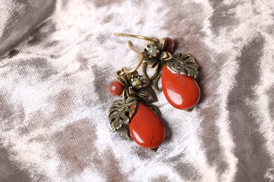 Photo of Beautiful pair of metal earrings with red jasper gemstones on light fabric