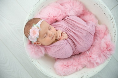 Adorable newborn girl lying in baby nest on light background, top view