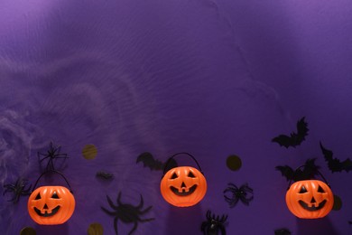 Flat lay composition with plastic pumpkin baskets, paper bats and spiders on purple background, space for text. Halloween decor