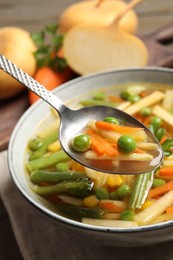 Photo of Spoon with delicious turnip soup above bowl at table, closeup