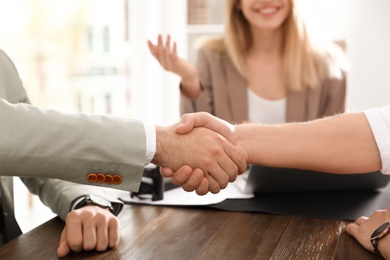 Business partners shaking hands at table after meeting in office, closeup