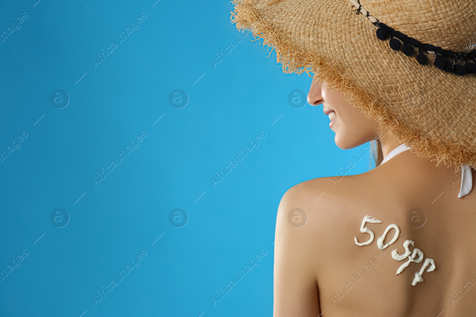 Photo of 50 SPF written with sun protection cream on woman's back against light blue background. Space for text