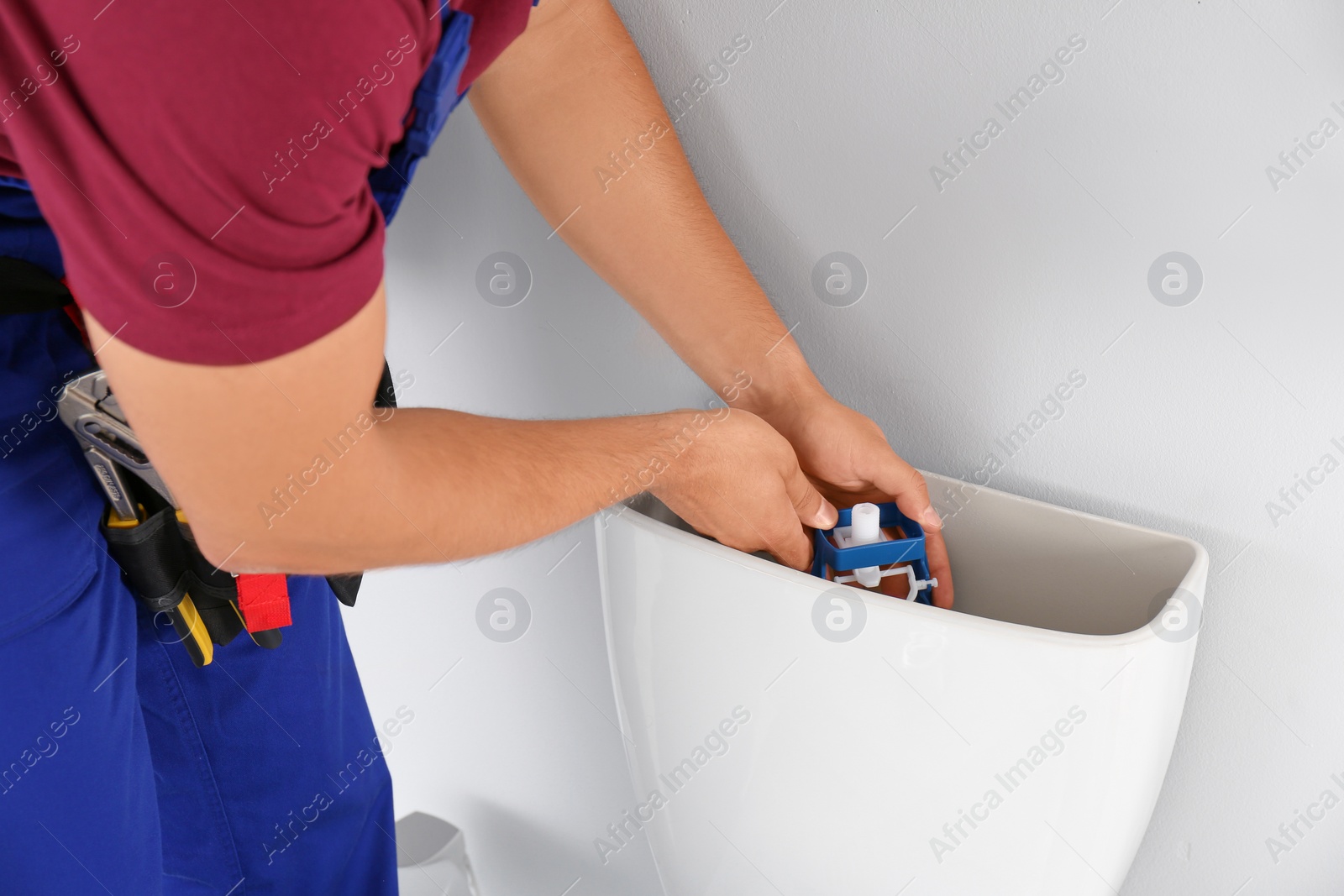 Photo of Young man working with toilet tank in bathroom, closeup