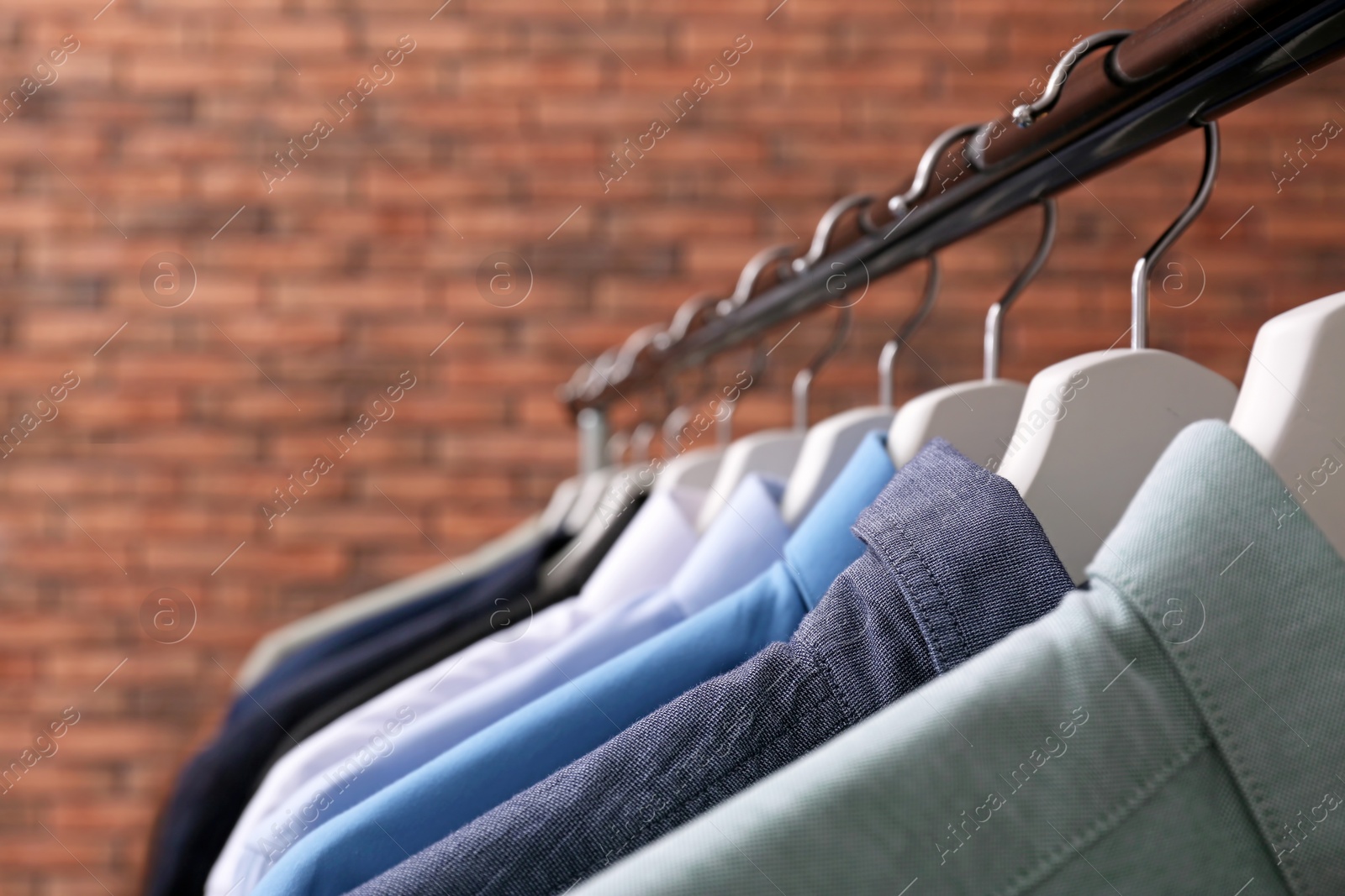 Photo of Wardrobe rack with stylish clothes near brick wall, closeup. Space for text