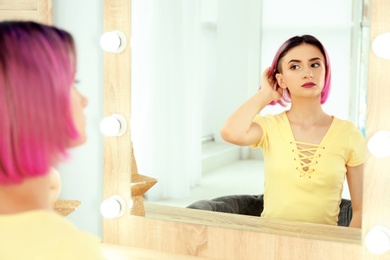 Young woman with color hair looking into mirror in beauty salon. Modern trend