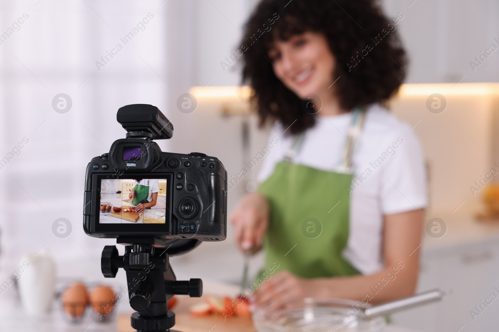 Photo of Food blogger cooking while recording video in kitchen, focus on camera