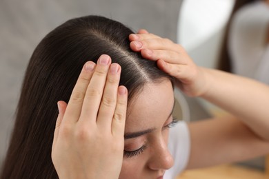 Woman examining her hair and scalp on blurred background, closeup