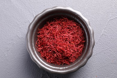 Photo of Aromatic saffron in bowl on gray textured table, top view