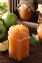 Photo of Glass jar of delicious apple jam and fresh fruits on wooden table, space for text