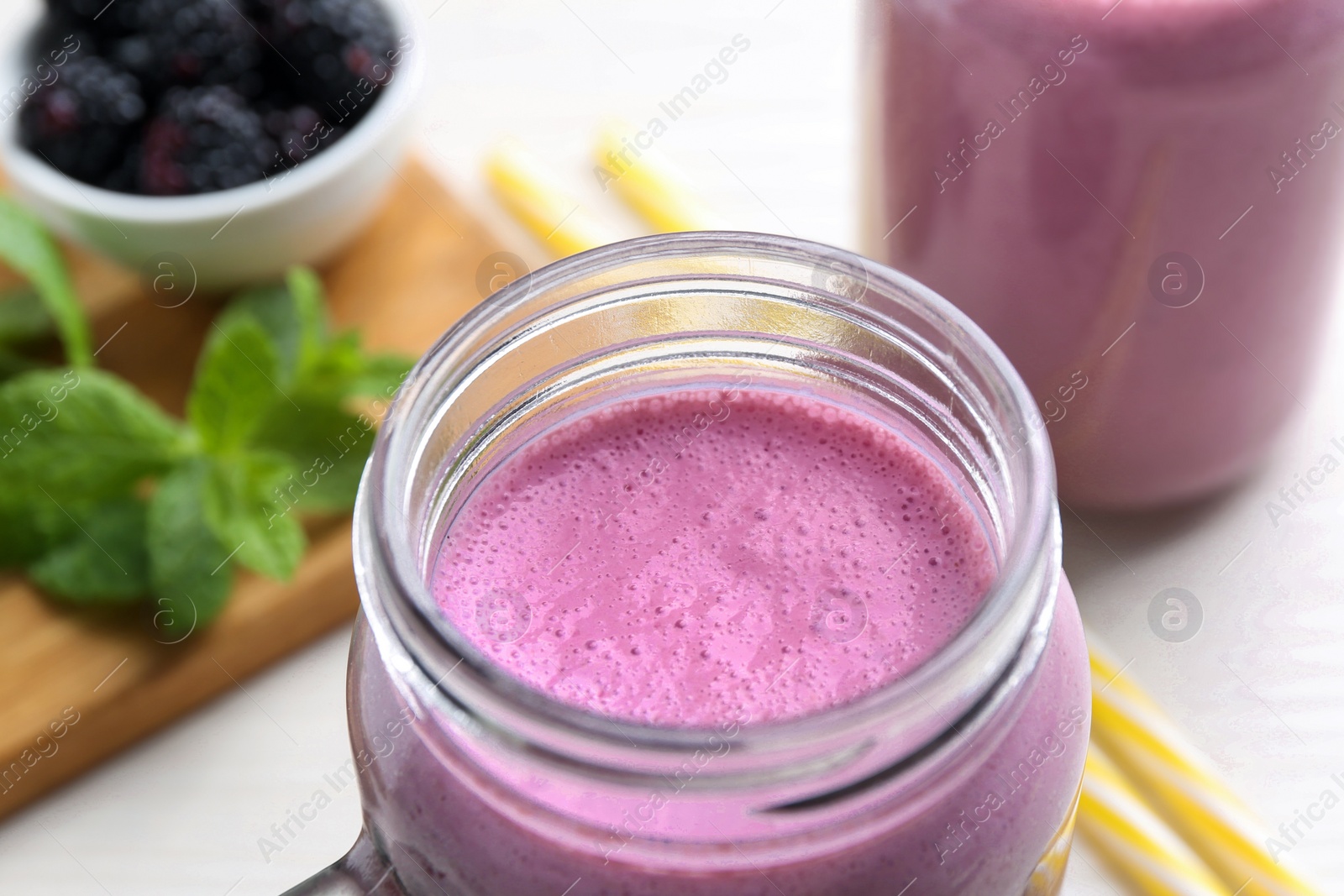 Photo of Mason jar of blackberry smoothie on white table, closeup