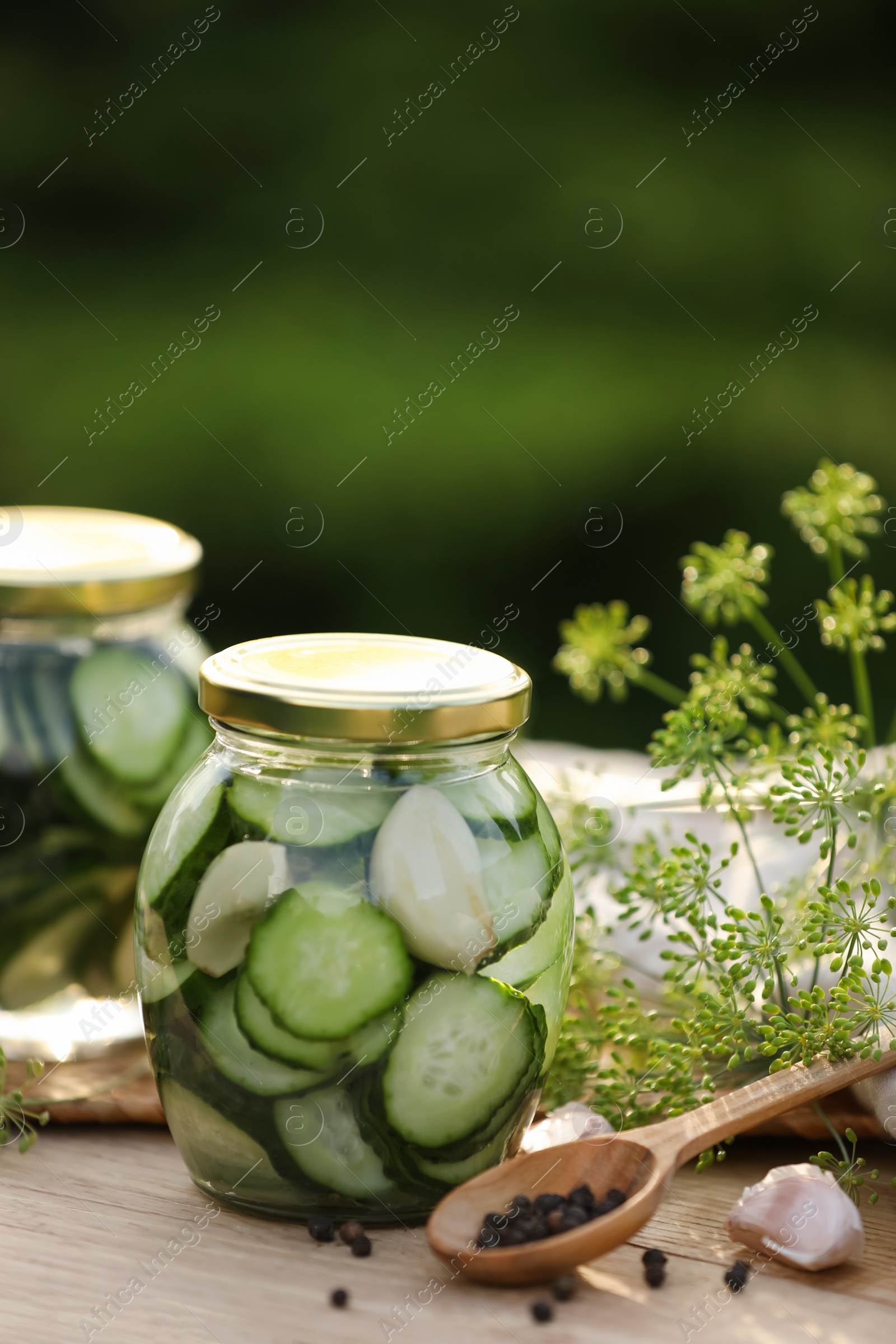 Photo of Jars of delicious pickled cucumbers and ingredients on wooden table against blurred background