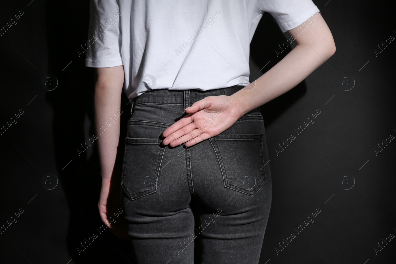 Photo of Woman showing open palm behind her back on black background, back view