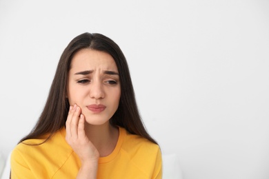 Photo of Young woman suffering from strong tooth pain on light background, space for text