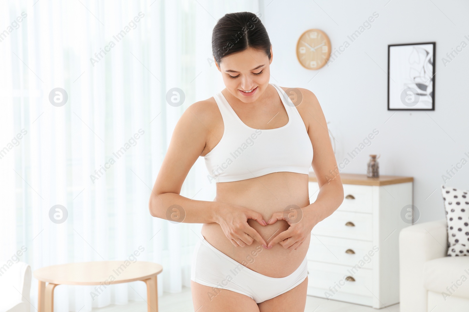 Photo of Beautiful pregnant woman showing heart with hands at home