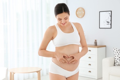 Beautiful pregnant woman showing heart with hands at home