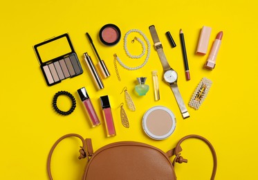 Stylish leather handbag, accessories and makeup items on yellow background, flat lay