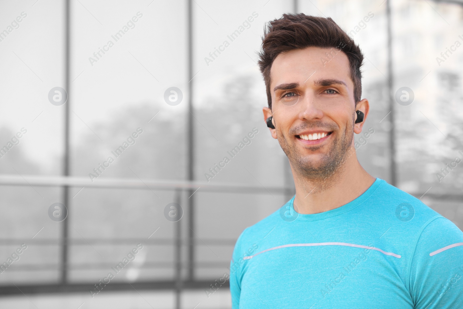 Photo of Young sportsman with wireless earphones on city street