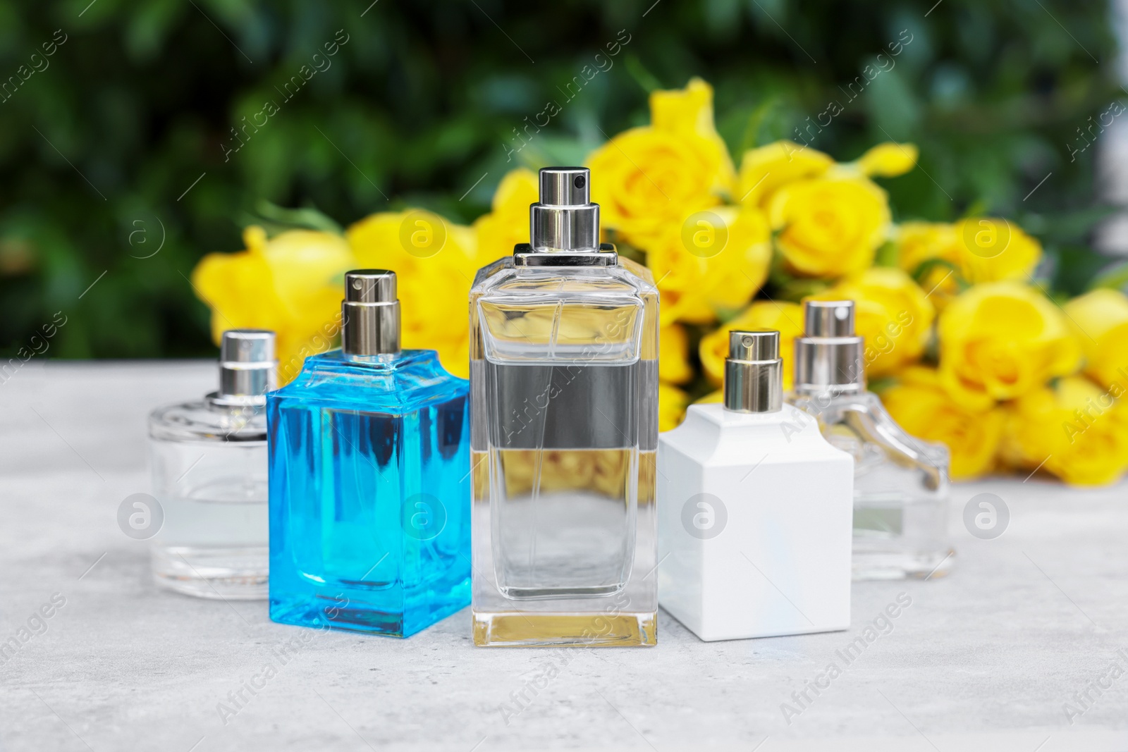 Photo of Perfumes and beautiful bouquet of yellow roses on light table outdoors, selective focus