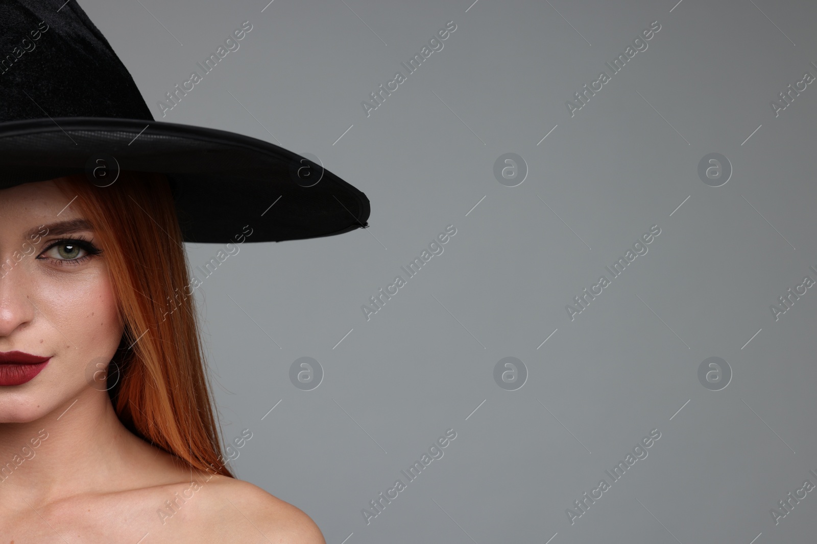 Photo of Young woman with witch hat on light grey background, closeup and space for text. Halloween celebration