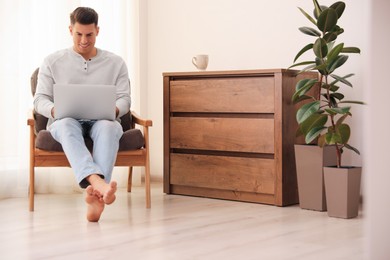Man with laptop sitting in armchair at home. Floor heating system