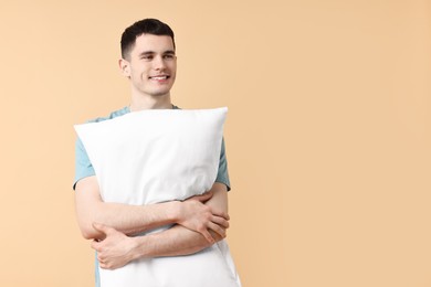 Photo of Happy man in pyjama holding pillow on beige background, space for text