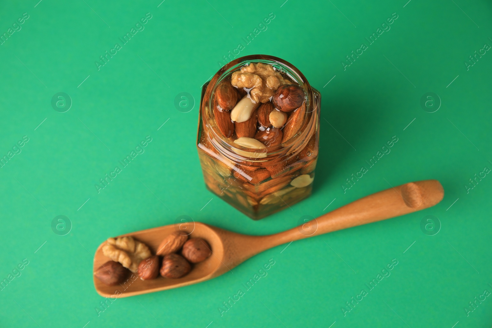 Photo of Different tasty nuts with honey on green background, above view