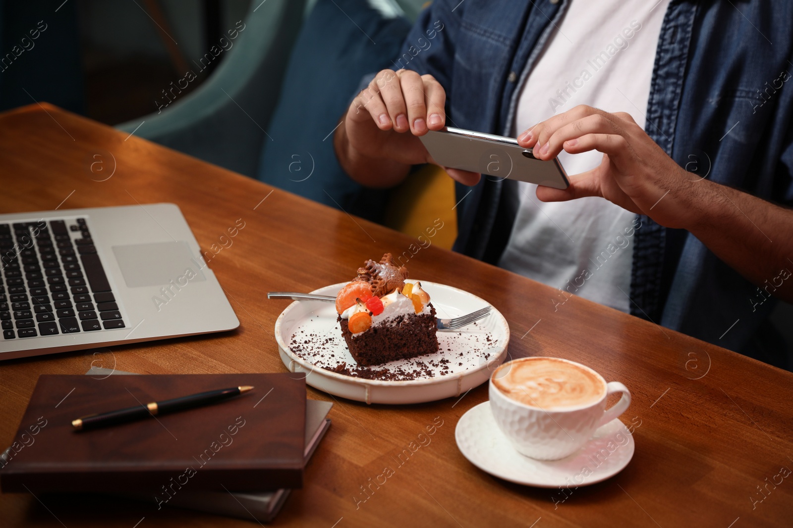 Photo of Young blogger taking picture of dessert at table in cafe, closeup