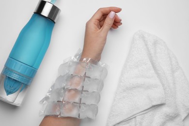 Woman with ice pack, bottle of water and towel on white background, top view. Heat stroke treatment