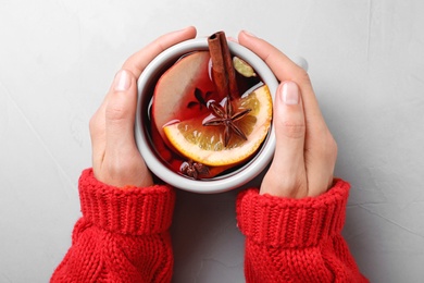 Photo of Woman holding cup of tasty mulled wine at grey table, top view