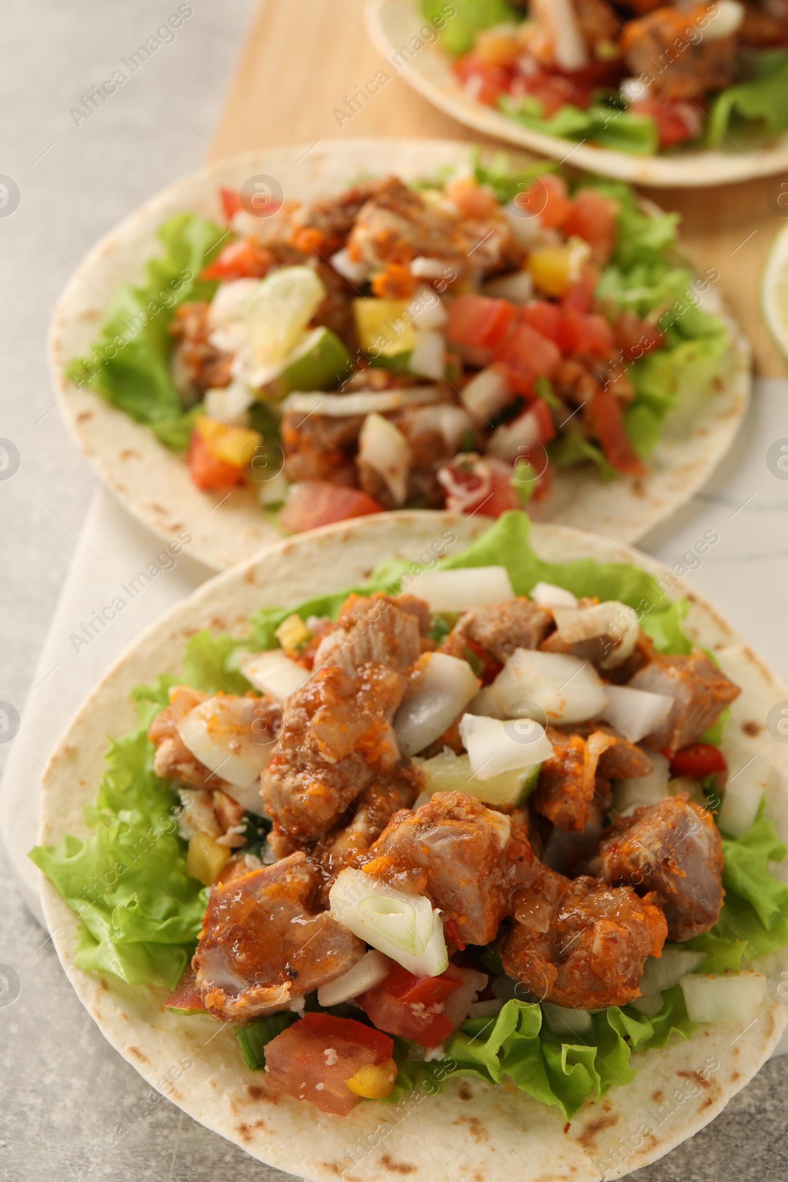 Photo of Delicious tacos with vegetables and meat on light table, closeup