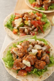 Delicious tacos with vegetables and meat on light table, closeup