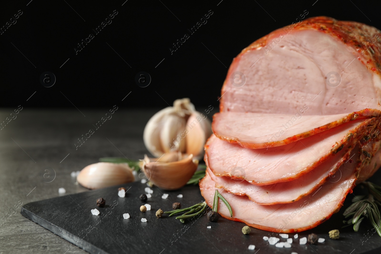 Photo of Slate plate with delicious ham on grey table against black background, closeup. Space for text