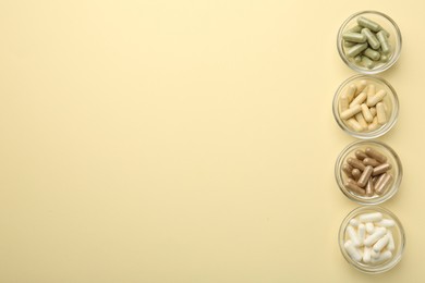 Photo of Different vitamin capsules in bowls on pale yellow background, flat lay. Space for text