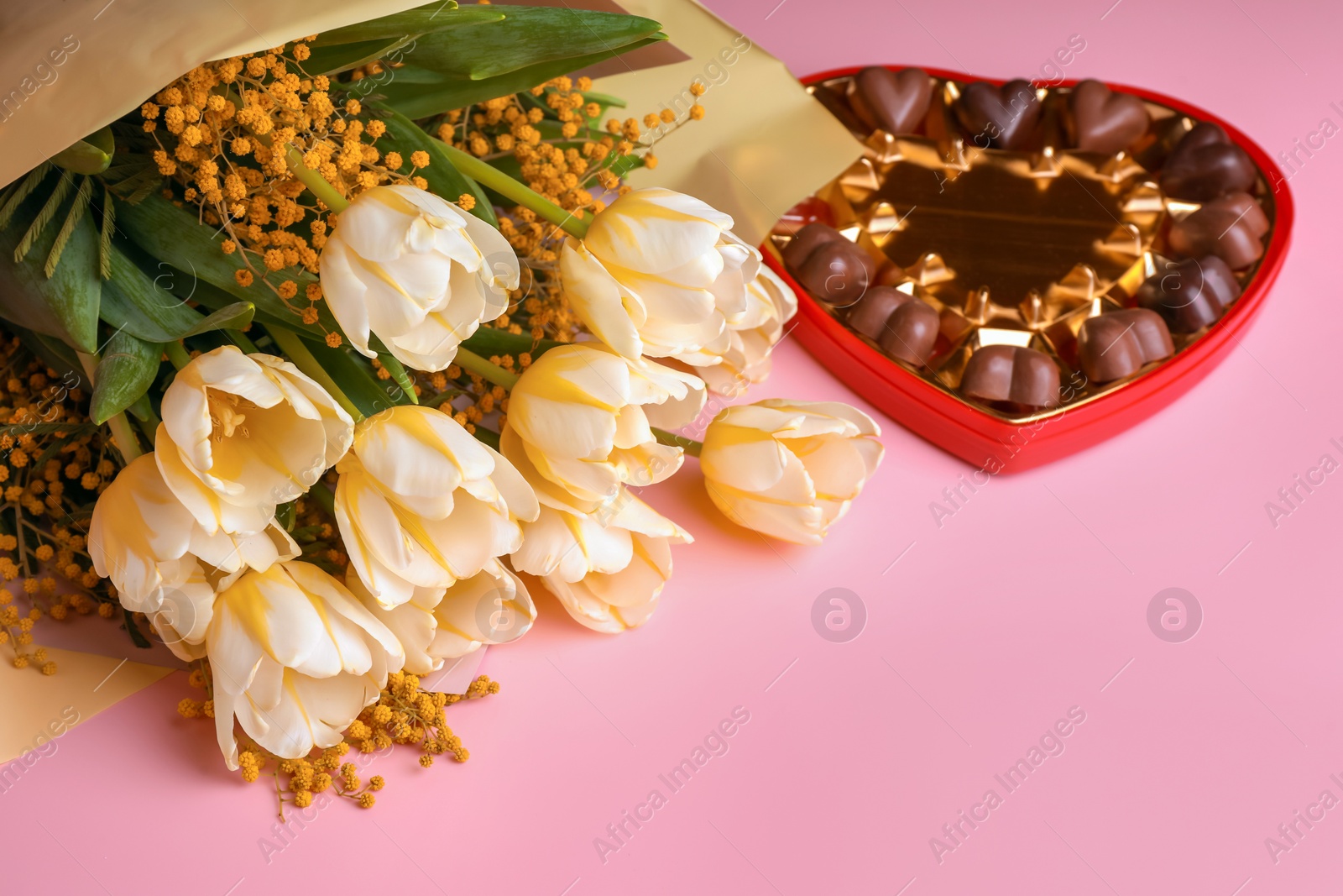 Photo of Bouquet with beautiful tulips, mimosa flowers and box of chocolate candies in shape of heart on pink background