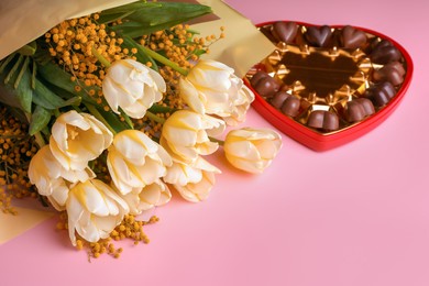 Bouquet with beautiful tulips, mimosa flowers and box of chocolate candies in shape of heart on pink background