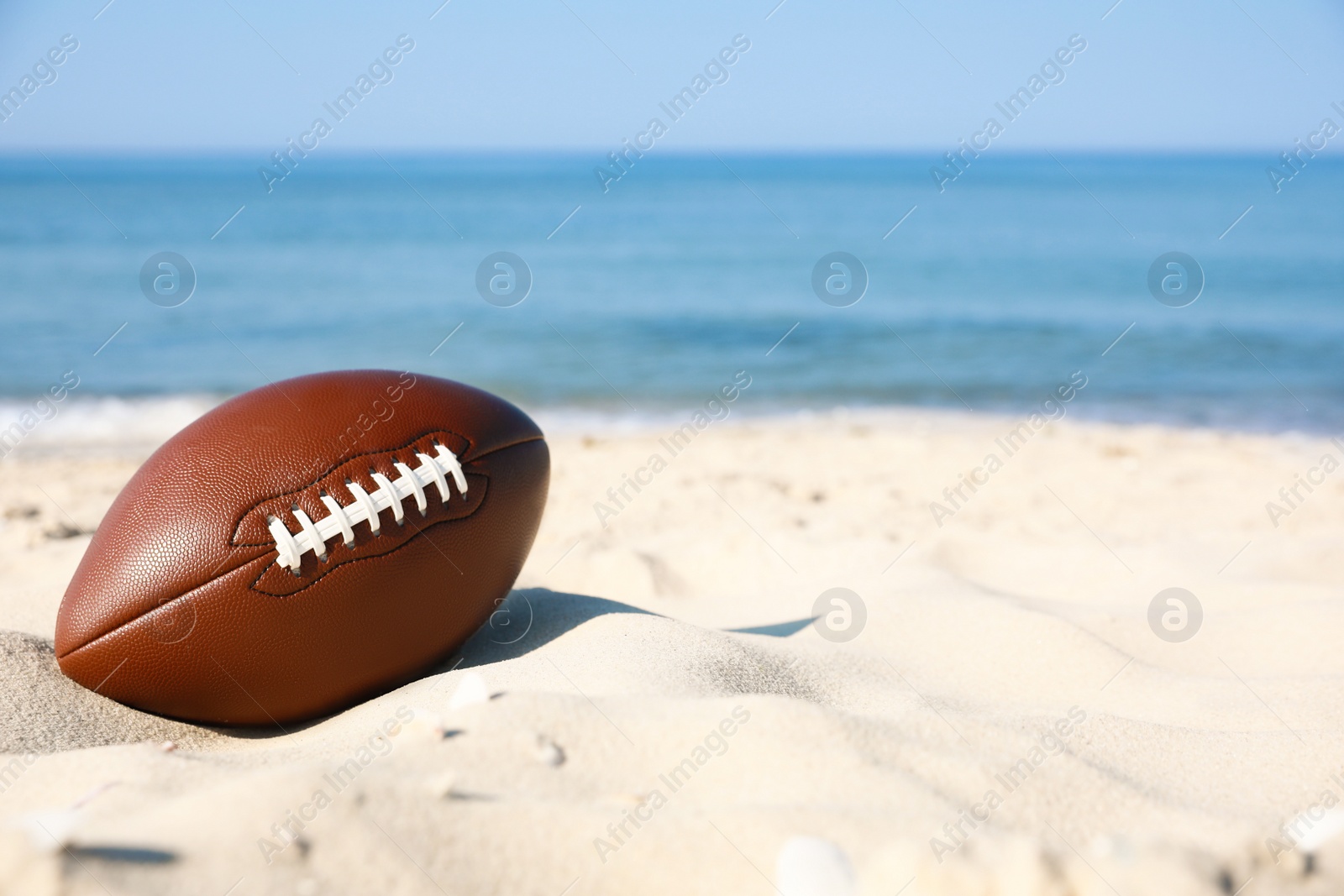 Photo of American football ball on beach. Space for text