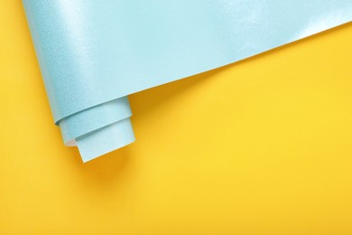 Photo of Roll of turquoise wrapping paper on yellow background, top view. Space for text