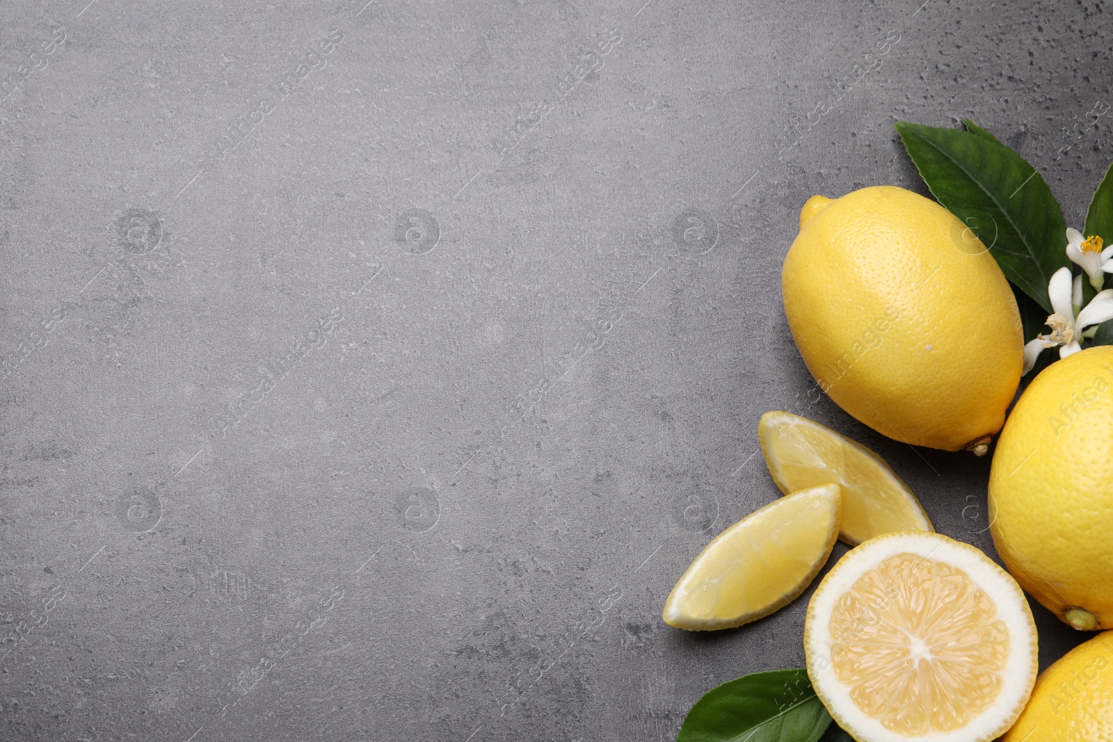 Photo of Many fresh ripe lemons with green leaves and flowers on grey table, flat lay. Space for text