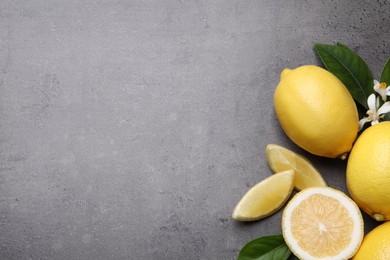 Many fresh ripe lemons with green leaves and flowers on grey table, flat lay. Space for text