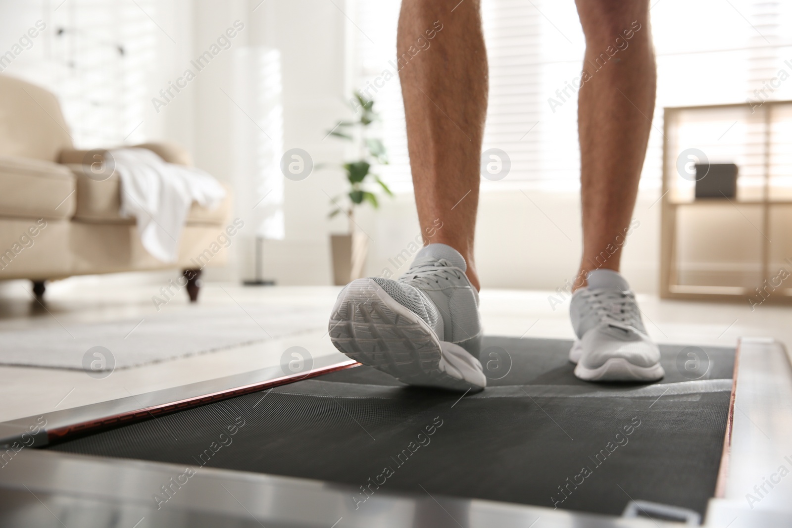 Photo of Sporty man training on walking treadmill at home, closeup