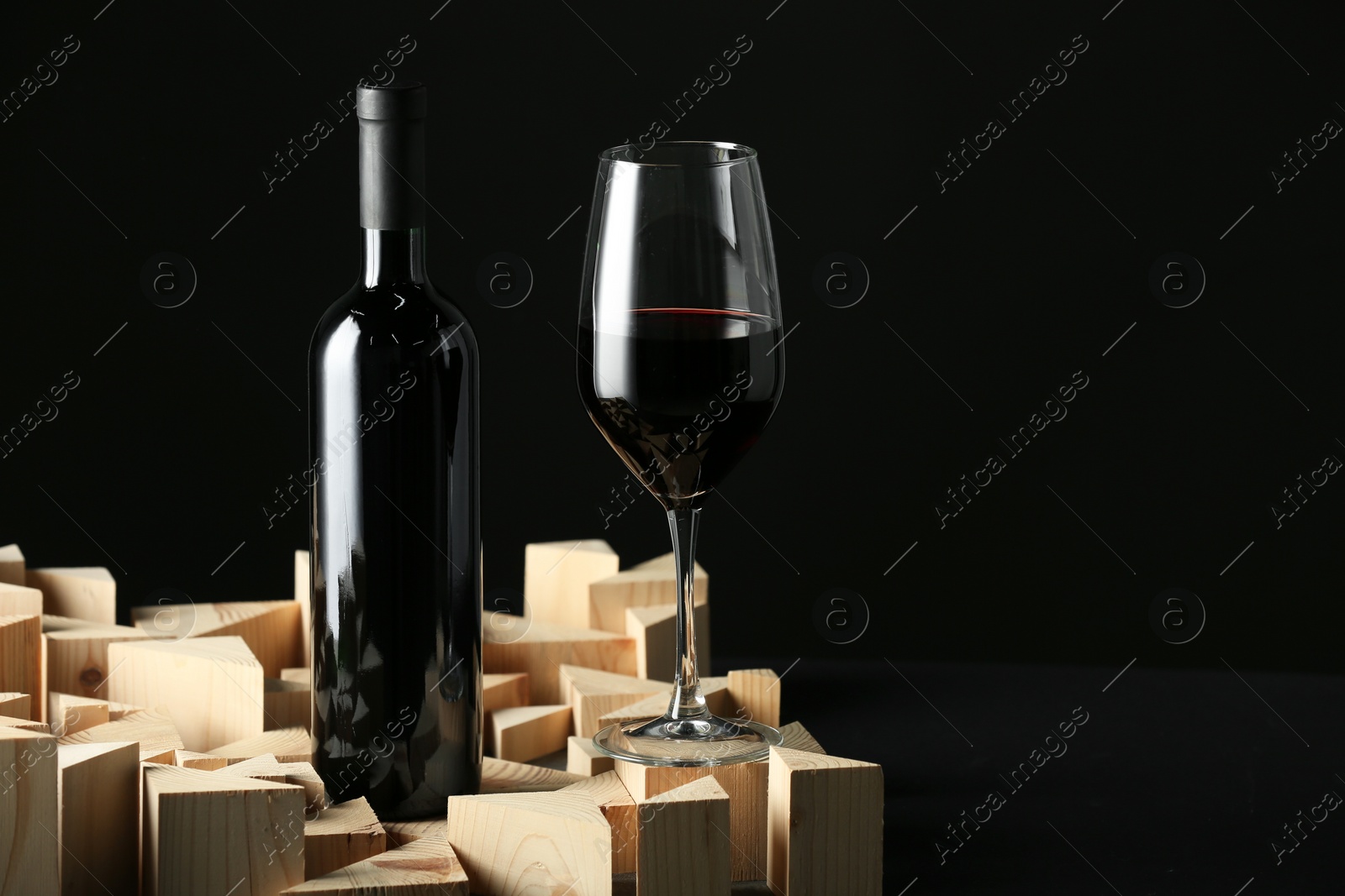 Photo of Stylish presentation of red wine in bottle and wineglass on black background, space for text