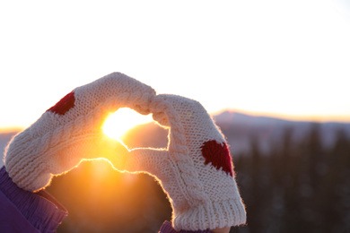 Woman making heart with her hands in mountains at sunset, closeup. Winter vacation