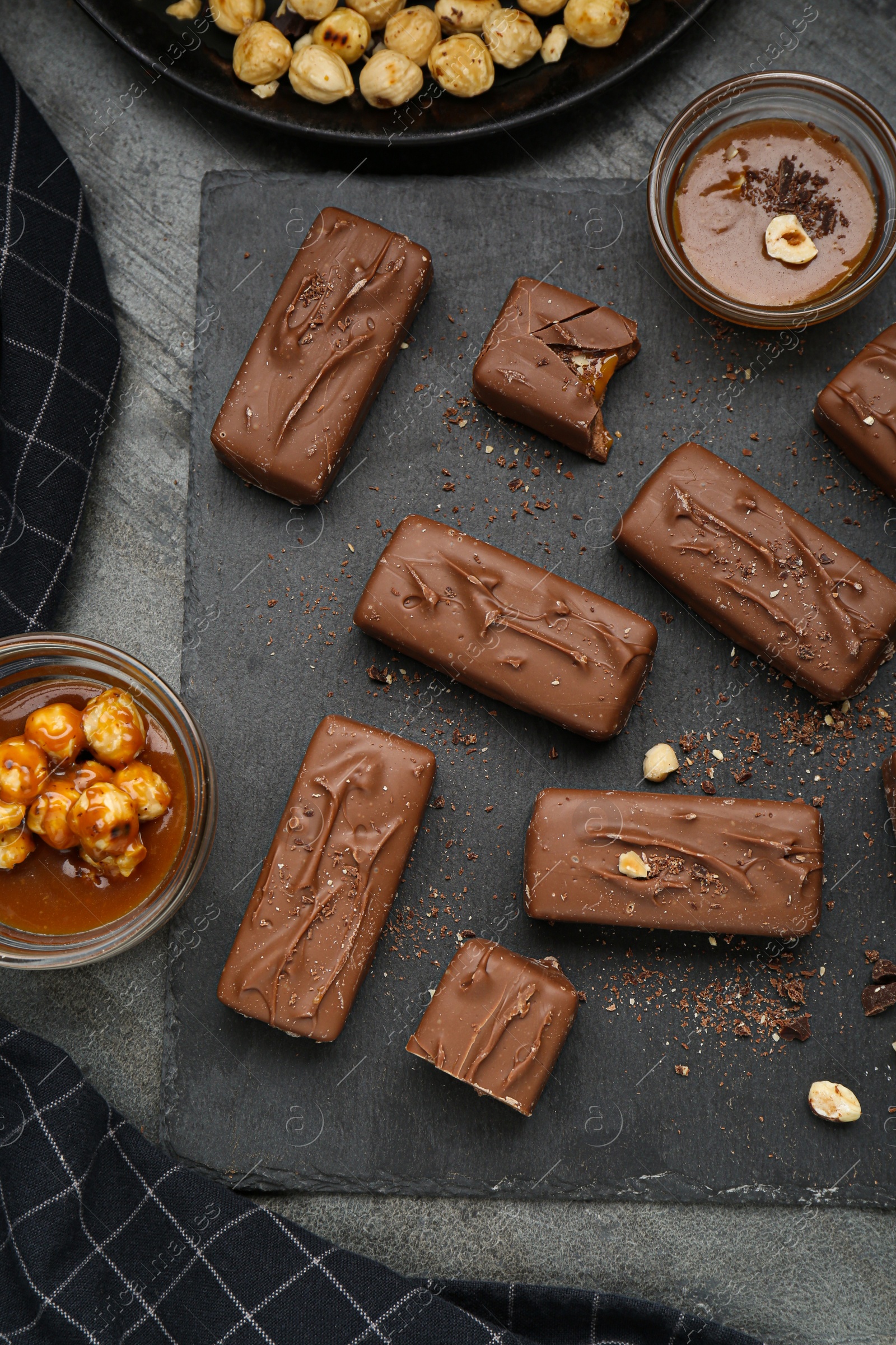 Photo of Delicious chocolate candy bars with caramel and nuts on grey table, flat lay